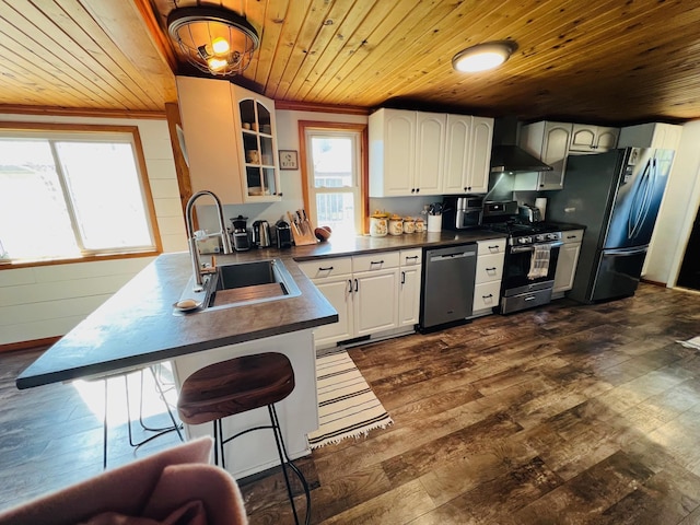kitchen featuring dark countertops, a sink, glass insert cabinets, wood ceiling, and stainless steel appliances
