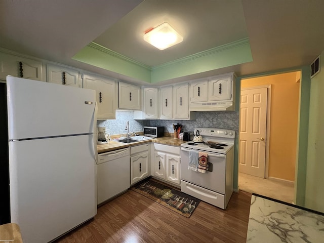 kitchen featuring white cabinets, a tray ceiling, a sink, white appliances, and under cabinet range hood