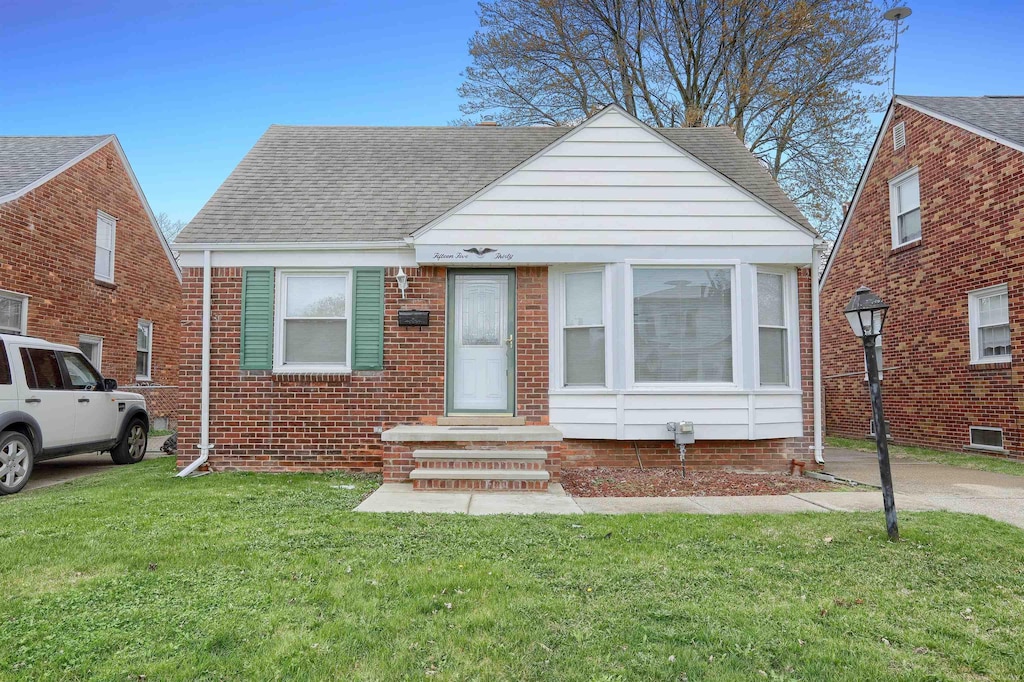 view of front of property with entry steps, a front lawn, roof with shingles, and brick siding