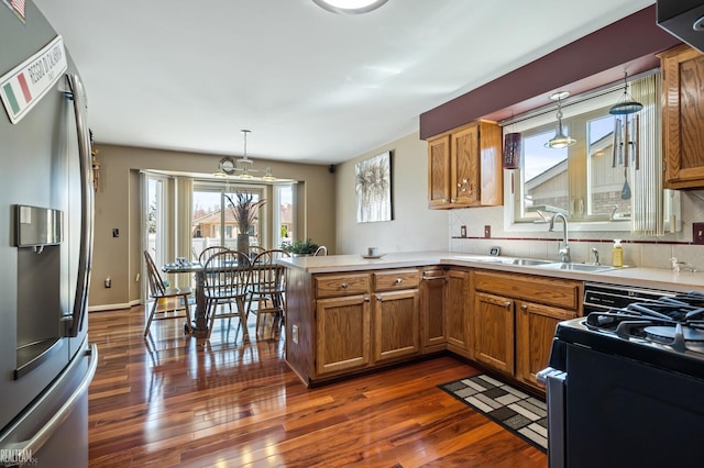 kitchen featuring dark wood finished floors, stainless steel fridge with ice dispenser, a sink, a peninsula, and brown cabinetry
