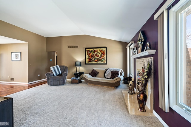living area with vaulted ceiling, visible vents, carpet flooring, and baseboards