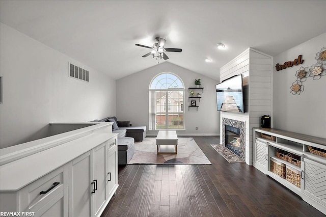 living room with dark wood finished floors, lofted ceiling, visible vents, a fireplace, and ceiling fan