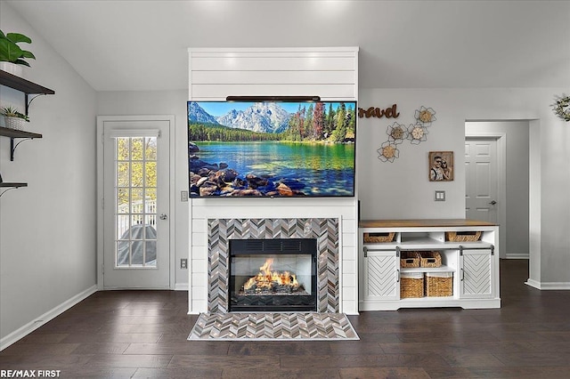 unfurnished living room featuring a tiled fireplace, baseboards, and wood finished floors