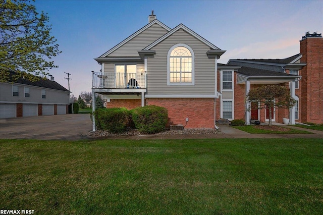 view of front of house with brick siding, a yard, and a balcony