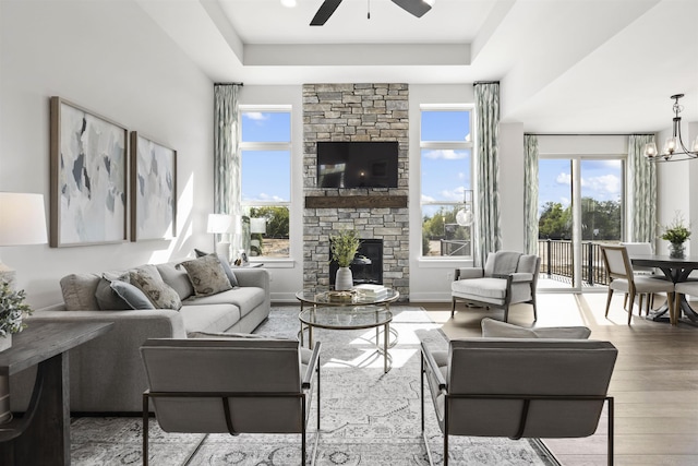 3897 Chatham Pl Unit 103, Brighton, MI 48114 - living room with a raised ceiling, a stone fireplace, wood finished floors, and ceiling fan with notable chandelier