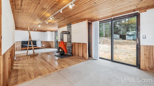 interior space with wood walls, a wood stove, rail lighting, wainscoting, and concrete floors