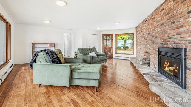 living room with baseboard heating, a baseboard radiator, a brick fireplace, and light wood-type flooring