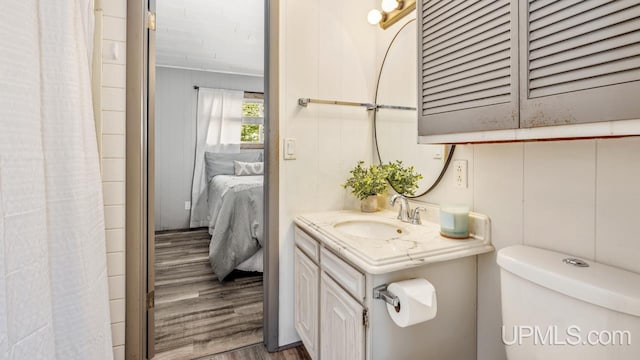 full bath with toilet, vanity, wood finished floors, and ensuite bathroom