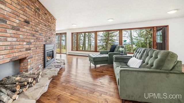 living room with a baseboard heating unit, wood finished floors, and a brick fireplace