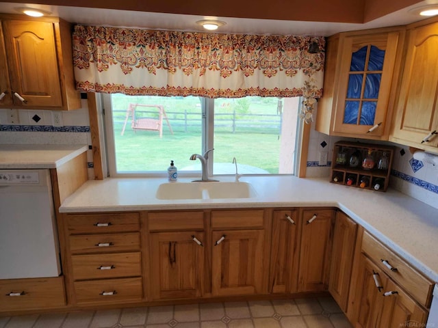 kitchen with light countertops, backsplash, dishwasher, and a sink