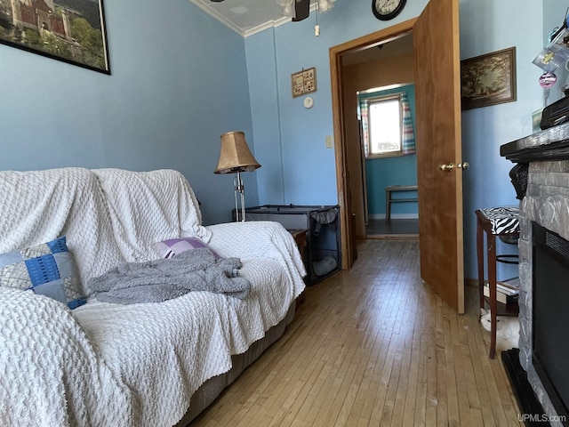 bedroom with a stone fireplace, baseboards, crown molding, and hardwood / wood-style floors