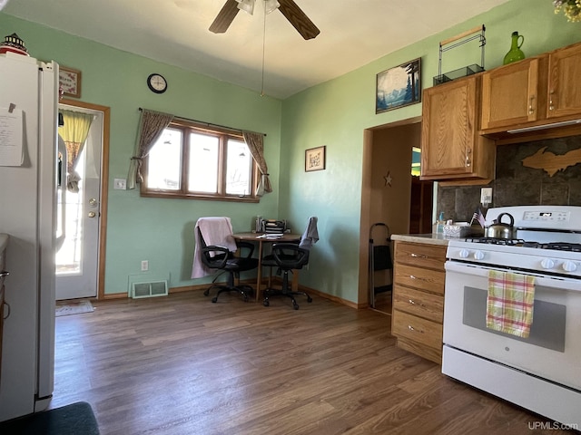 kitchen with brown cabinets, visible vents, a ceiling fan, white appliances, and dark wood-type flooring