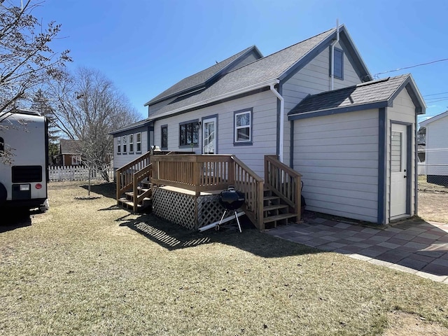 rear view of property featuring a wooden deck, roof with shingles, fence, and a yard