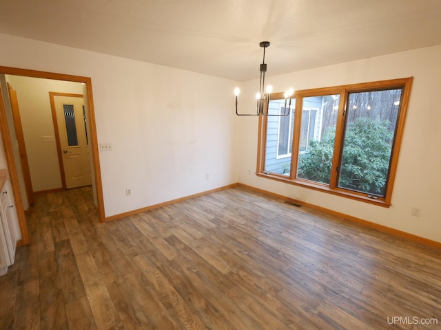 unfurnished dining area with an inviting chandelier, wood finished floors, visible vents, and baseboards