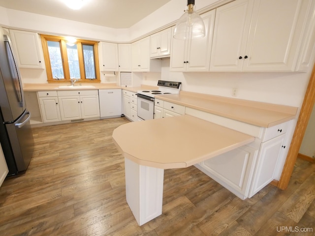 kitchen featuring white cabinets, a sink, wood-type flooring, white appliances, and a peninsula