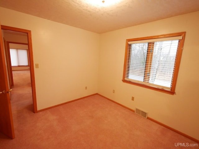 unfurnished room featuring light colored carpet, baseboards, a textured ceiling, and visible vents