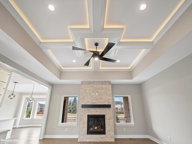 unfurnished living room featuring a stone fireplace, a wealth of natural light, a ceiling fan, and coffered ceiling