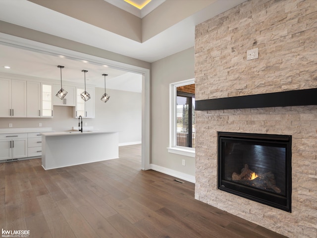 kitchen featuring white cabinets, a sink, baseboards, a fireplace, and dark wood-style flooring