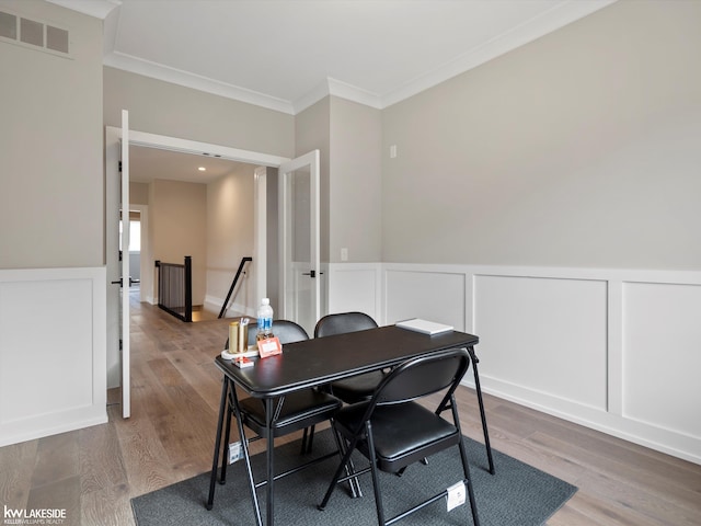 office with a decorative wall, wood finished floors, visible vents, and ornamental molding