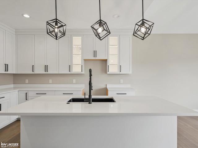 kitchen with white cabinets, light countertops, wood finished floors, a sink, and a kitchen island with sink