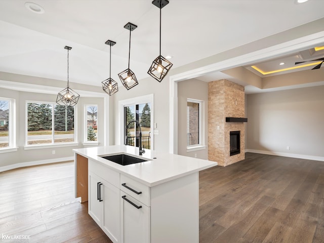 kitchen with a sink, open floor plan, a large fireplace, light countertops, and dark wood-type flooring