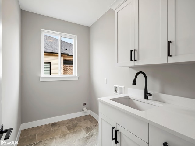 clothes washing area featuring a sink, baseboards, washer hookup, stone finish floor, and cabinet space
