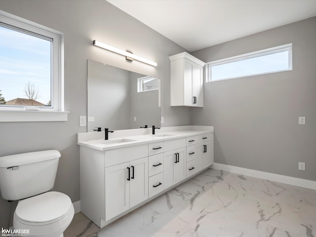 bathroom with a sink, double vanity, toilet, baseboards, and marble finish floor
