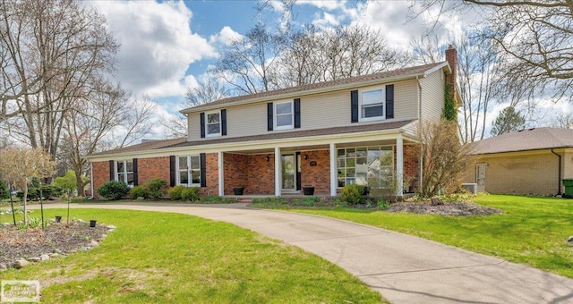 traditional home with a chimney, a front lawn, brick siding, and a porch