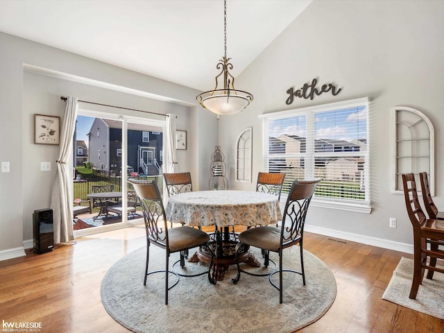 dining area featuring high vaulted ceiling, light wood-type flooring, and baseboards