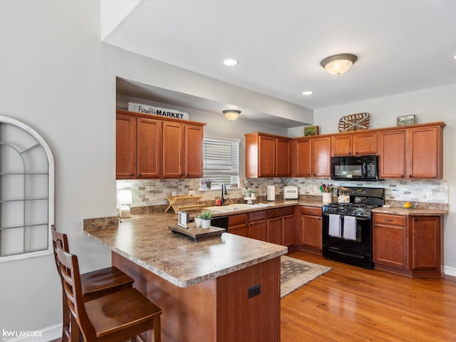 kitchen with a kitchen breakfast bar, a sink, black appliances, a peninsula, and brown cabinetry