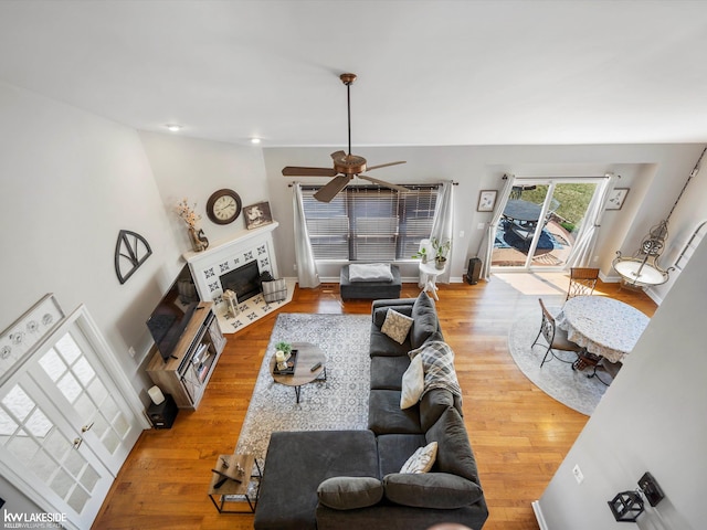 living area featuring a tiled fireplace, wood finished floors, and ceiling fan