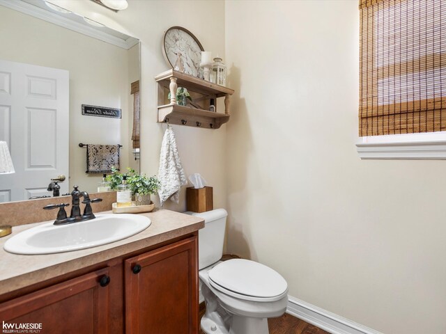 half bath with baseboards, toilet, vanity, and wood finished floors