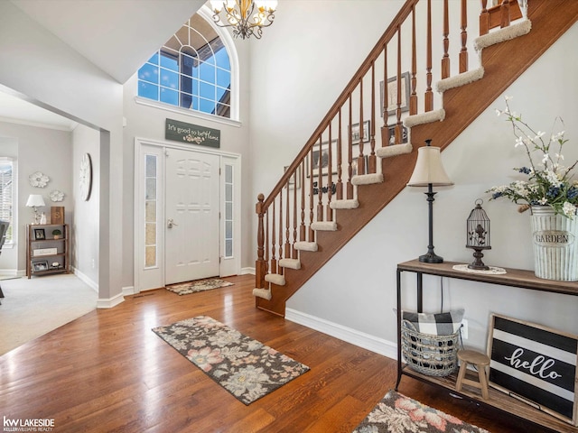 foyer entrance with stairway, a high ceiling, an inviting chandelier, wood finished floors, and baseboards