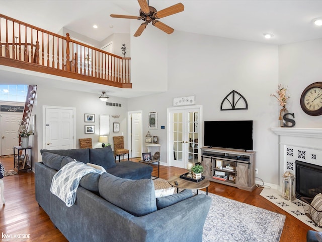 living room with a tile fireplace, wood finished floors, visible vents, high vaulted ceiling, and ceiling fan