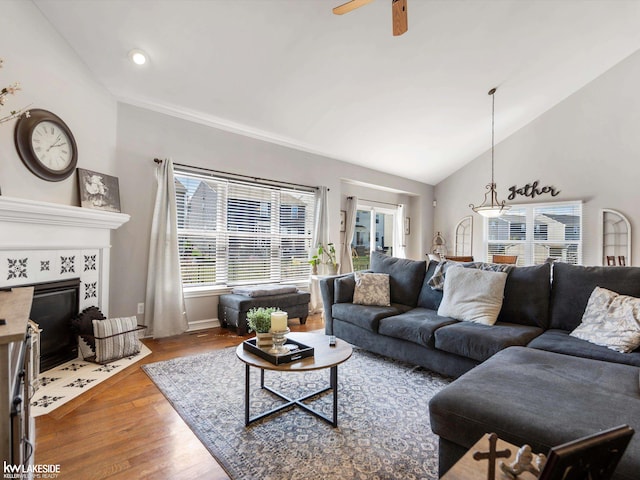living room with lofted ceiling, wood finished floors, a ceiling fan, baseboards, and a tiled fireplace