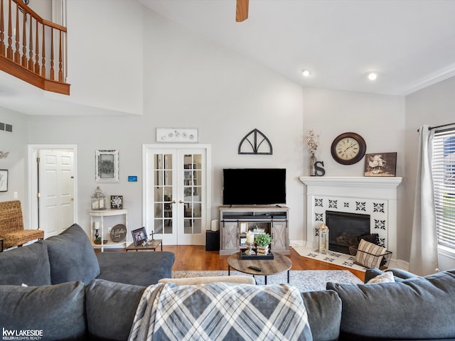 living area with wood finished floors, french doors, a tile fireplace, a high ceiling, and visible vents