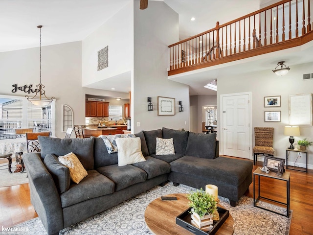 living room with visible vents, baseboards, wood finished floors, and high vaulted ceiling
