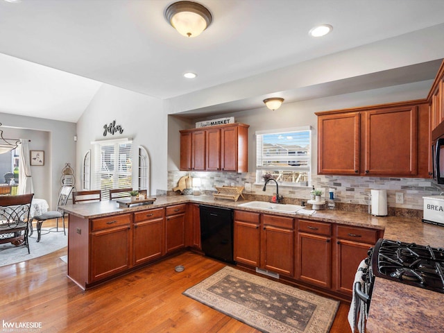 kitchen with a peninsula, a healthy amount of sunlight, a sink, and black appliances