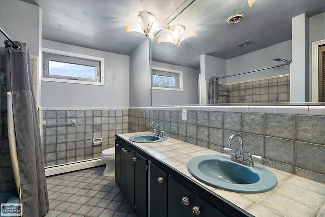 bathroom featuring baseboard heating, a sink, visible vents, and tile walls