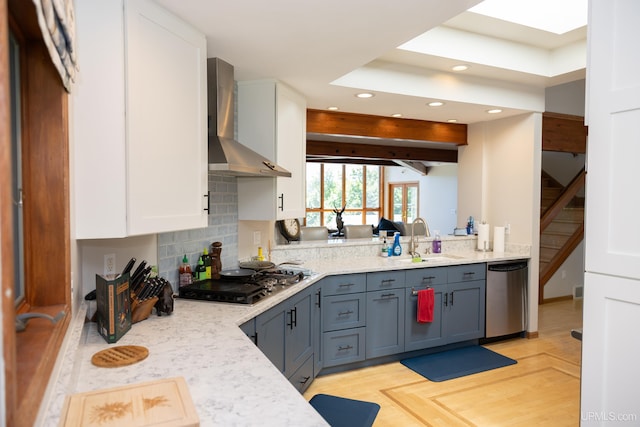 kitchen featuring wall chimney range hood, a sink, stainless steel appliances, white cabinets, and recessed lighting