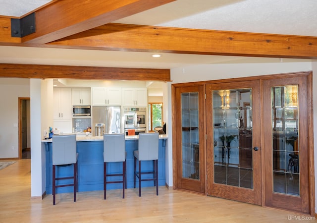 kitchen featuring a kitchen breakfast bar, beam ceiling, light wood-style flooring, appliances with stainless steel finishes, and white cabinetry