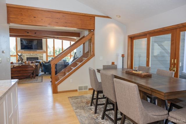dining room featuring stairway, light wood-style floors, a fireplace, lofted ceiling, and visible vents