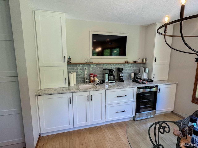bar featuring a textured ceiling, a sink, decorative backsplash, light wood-type flooring, and wine cooler