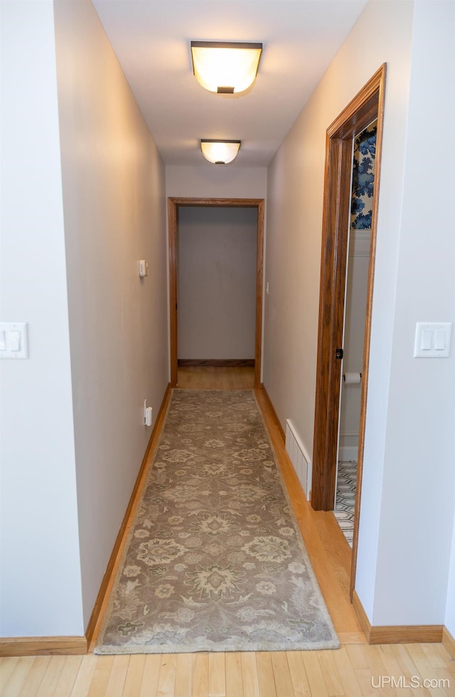 hall featuring light wood-style flooring, visible vents, and baseboards