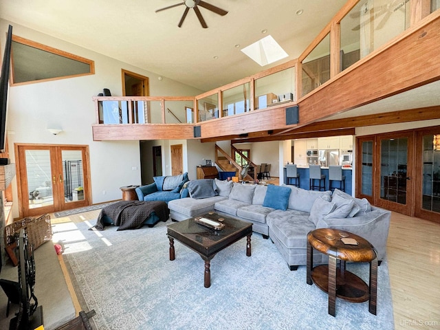 living room with a towering ceiling, a skylight, a ceiling fan, and french doors