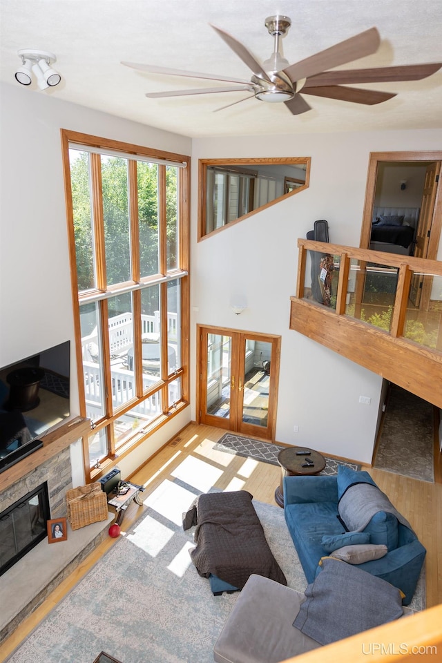 living area featuring french doors, a ceiling fan, wood finished floors, and a stone fireplace
