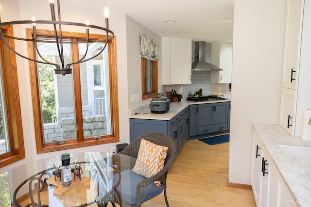 kitchen with white cabinets, stainless steel gas cooktop, tasteful backsplash, light wood-type flooring, and wall chimney range hood
