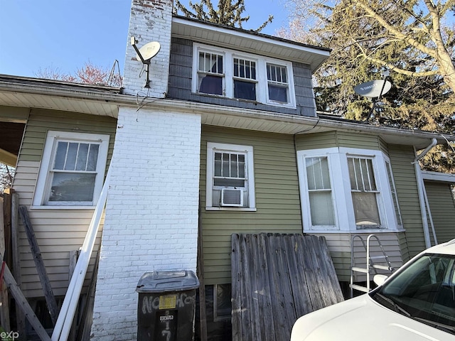 view of side of home with a chimney, brick siding, and cooling unit