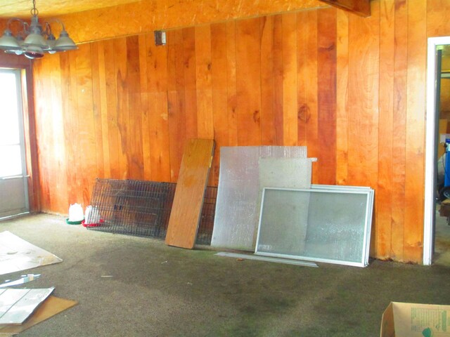 unfurnished living room with an inviting chandelier, wood walls, and carpet floors