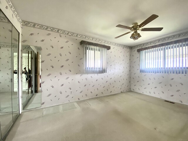 carpeted spare room with wallpapered walls, visible vents, and ceiling fan